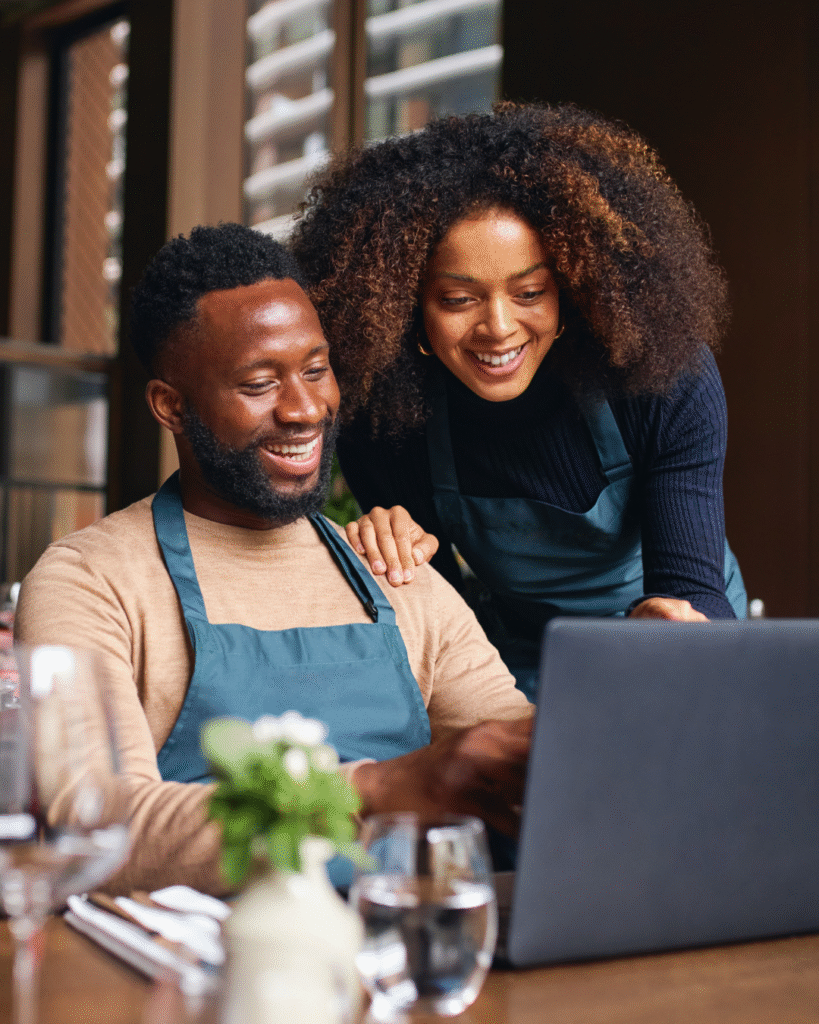 Two people smiling while using a laptop.